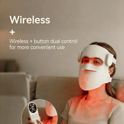 Woman using wireless red light therapy LED face mask with remote control on a sofa